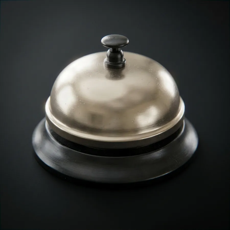 A hotel desk service bell in bone metal on a dark surface.